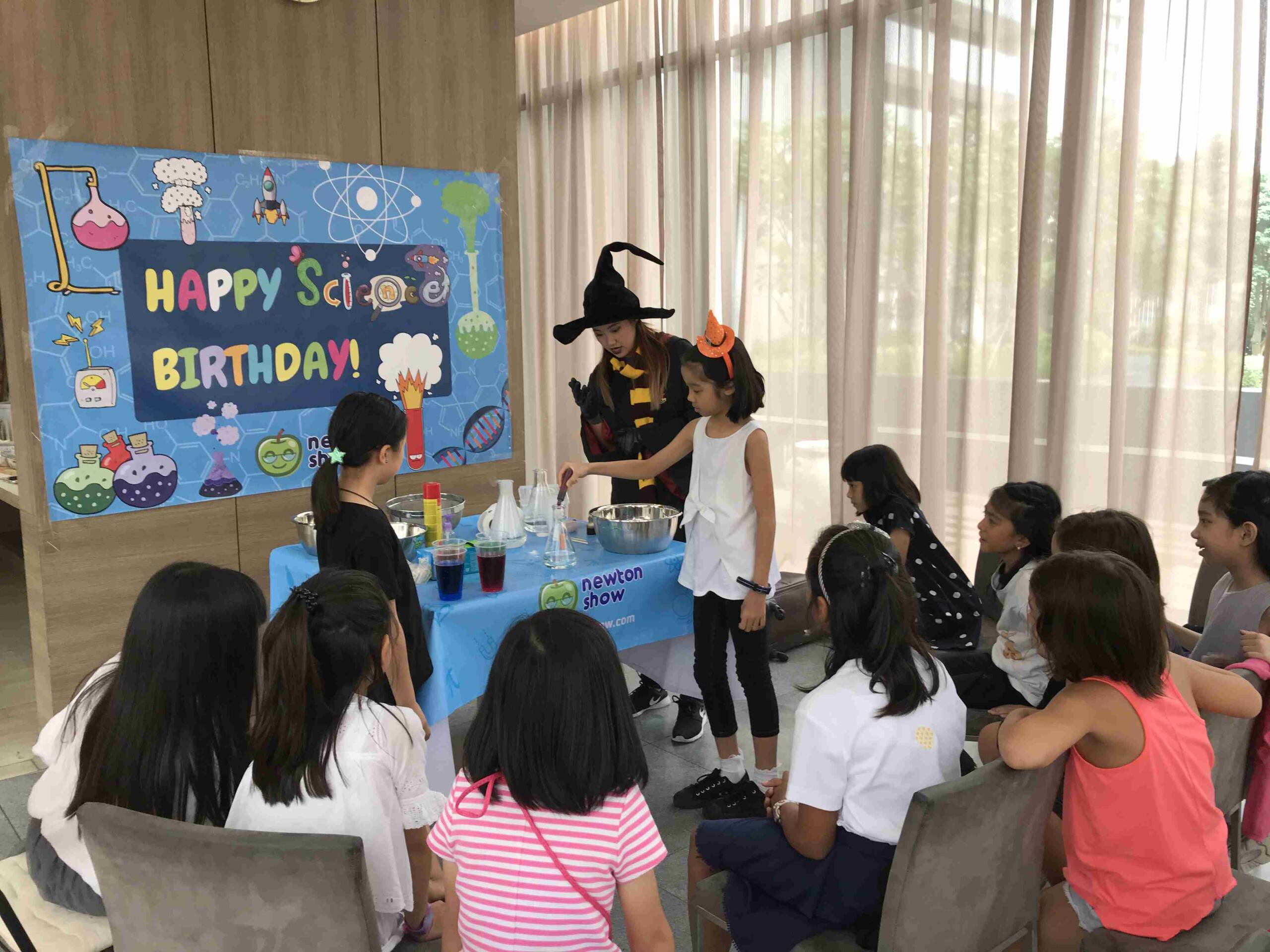Children watching a wizarding experiment in front of a Happy Birthday backdrop