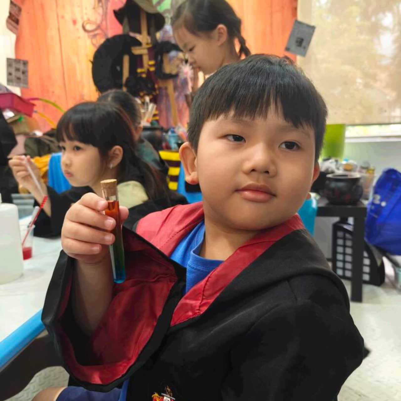 Boy in a wizard robe holding up the red potion he brewed at a Newtonshow birthday party in Hong Kong