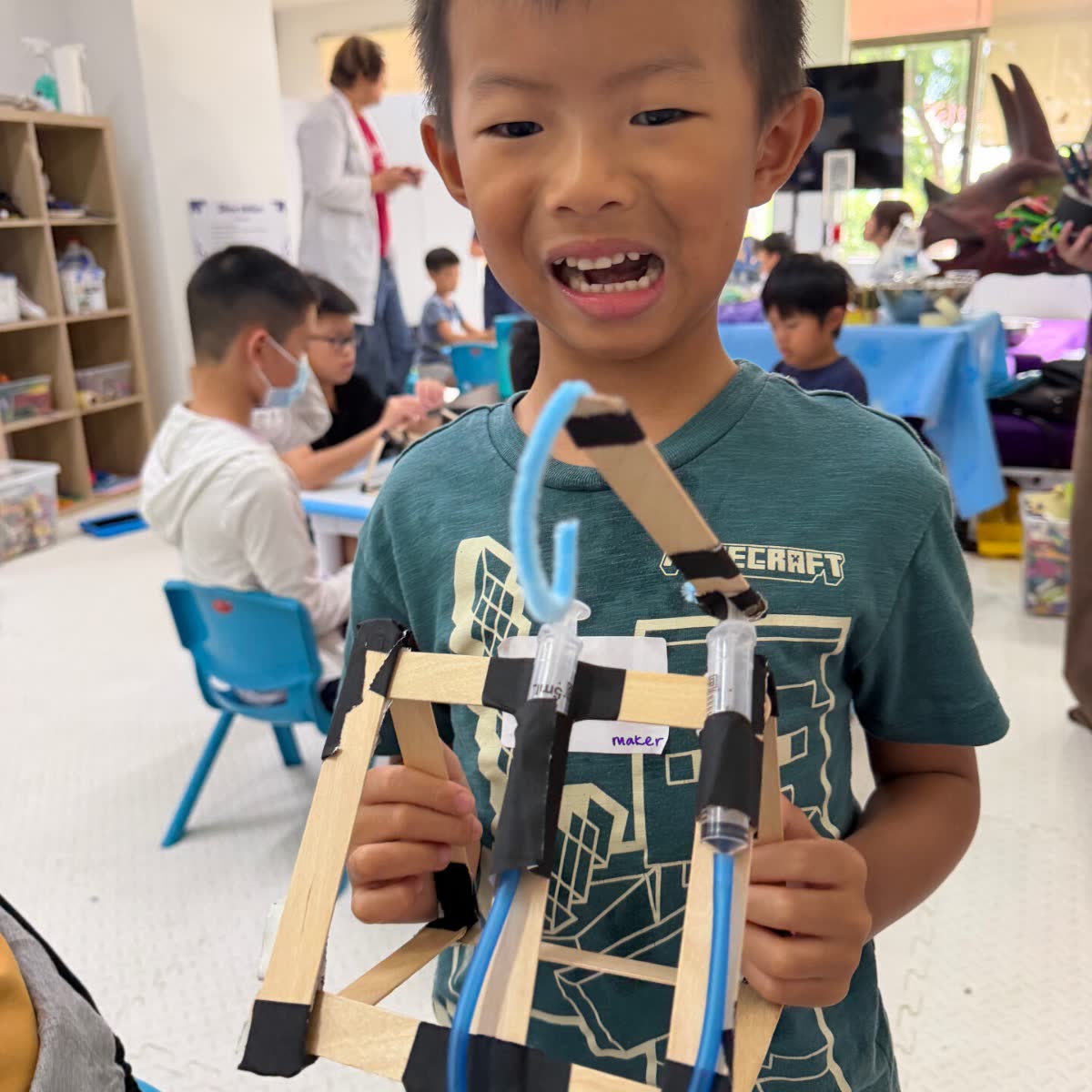 Smiling boy holding the wooden-stick structure he engineered at a Newtonshow Hong Kong camp